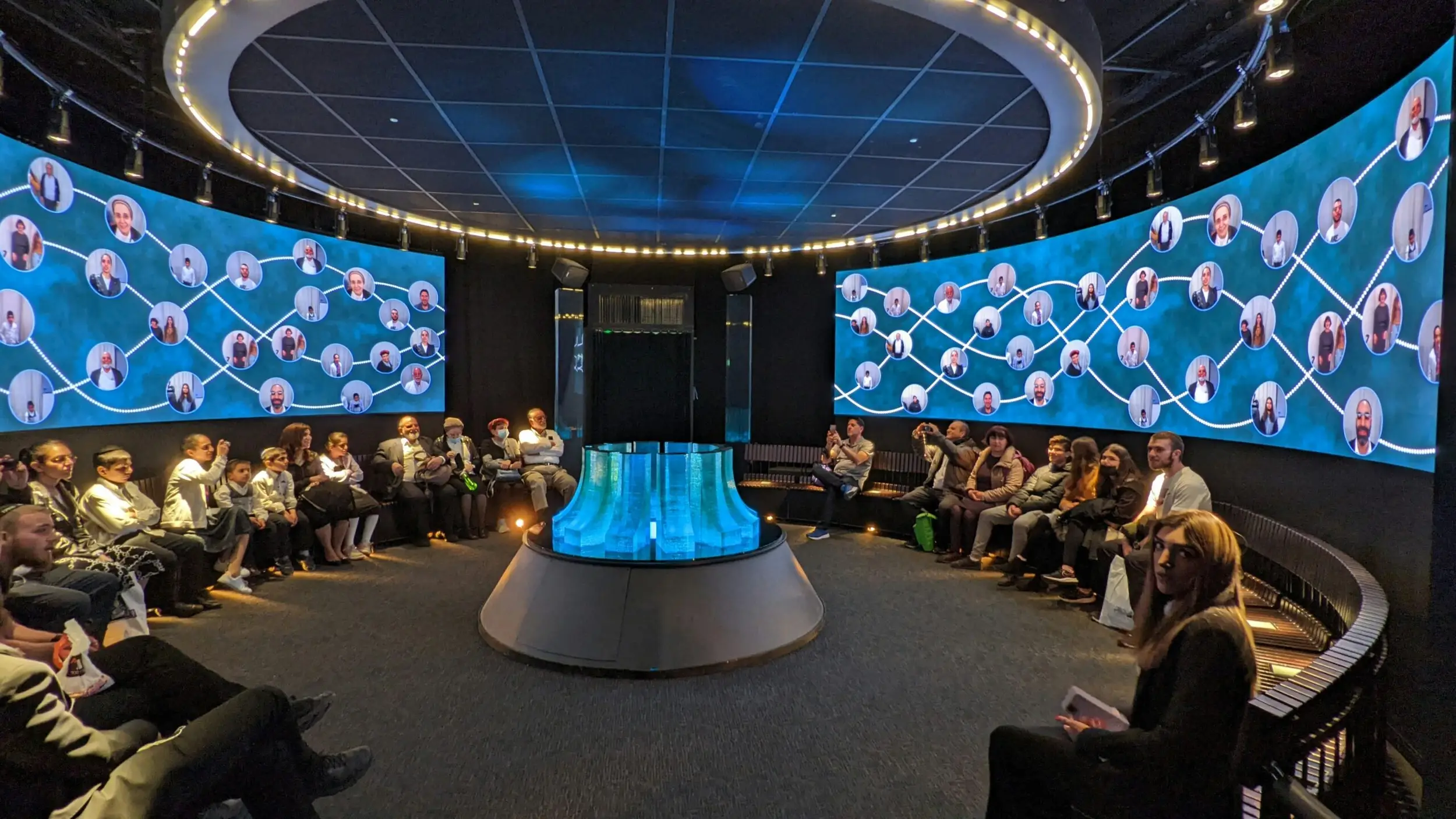 Audience members sit in a circular room surrounded by a panoramic screen displaying an event presentation enhanced by visually stunning designs